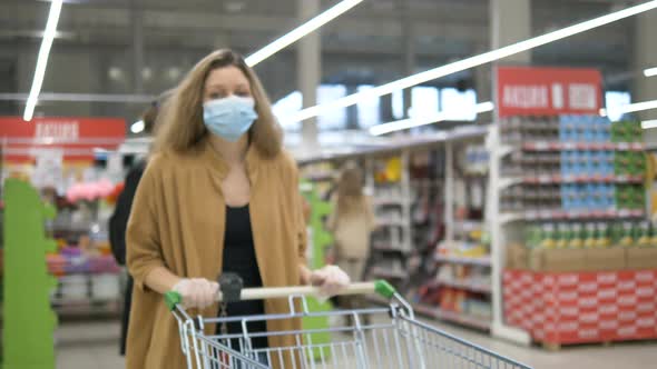 Girl in Protective Mask Rubber Gloves Walks in Supermarket with Trolley alt