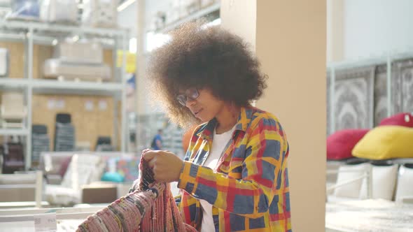 African American Woman with an Afro Hairstyle Chooses a Carpet in a Furniture Store alt