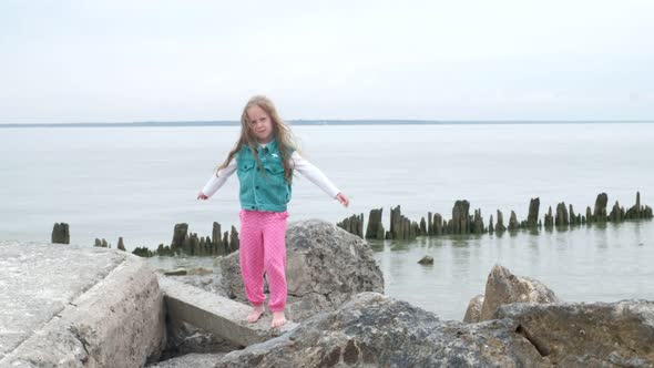 Girl Preschooler Plays on Large Stones on the Seashore.