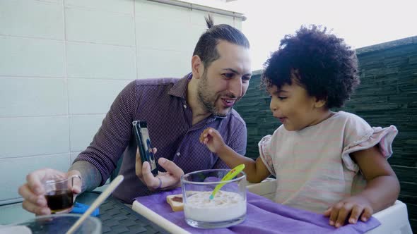 Slow motion shot of girl in high chair watching video on smartphone alt