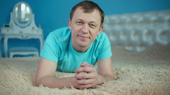 Smiling young man lying on bed in bedroom and looking at camera alt
