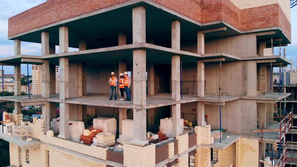 Three Construction Workers Talk While Standing on a Site. Multiethnic Engineers, Architects alt