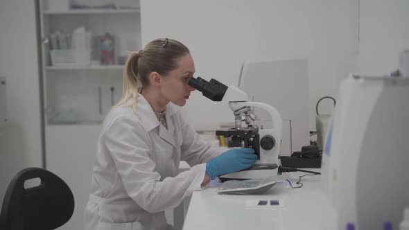 Female Medical Professional Works with Samples and Analyzes in Medical Laboratory Behind Microscope alt