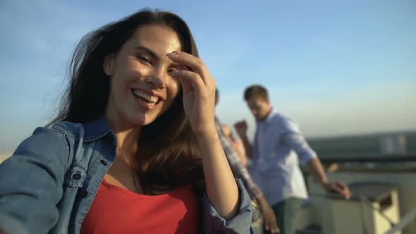 Brunette Girl Recording Video at Roof Party, Friends Dancing on Background