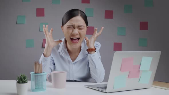 Asian woman working on a laptop angry shouting at home office