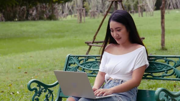 Young Asian woman using laptop at a public park.