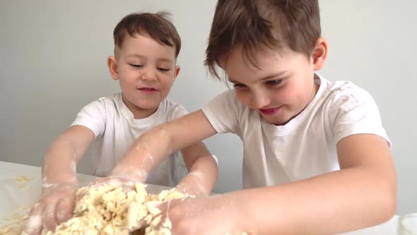 Two Small Children Prepare Something From the Dough. A Two Boys Are Sitting at the Kitchen Table.