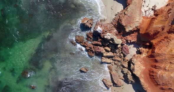 waves crashing agains red rock on the beach alt
