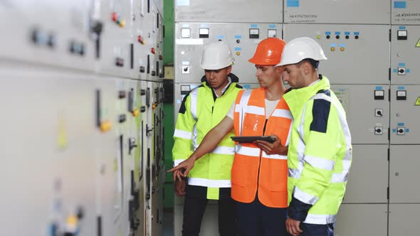 Engineers in Uniform and Helmets With Digital Tablet Works Inspecting Electrical Station