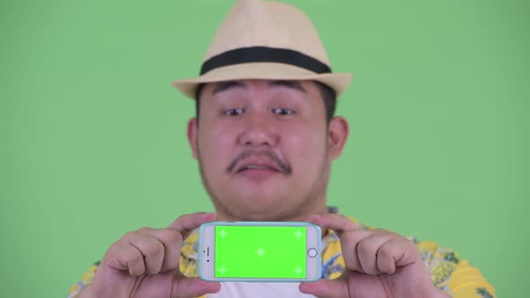 Face of Happy Young Overweight Asian Tourist Man Showing Phone alt