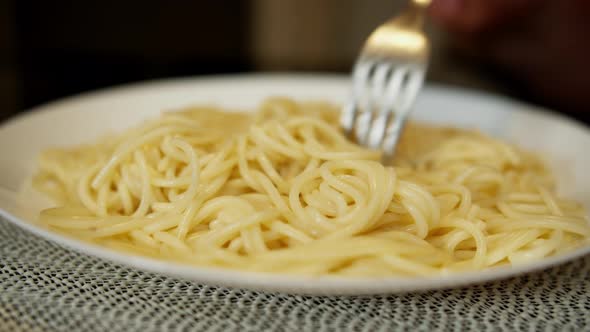 Plate full of freshly cooked hot spaghetti, steam comes, a man winds spaghetti on a fork and eats