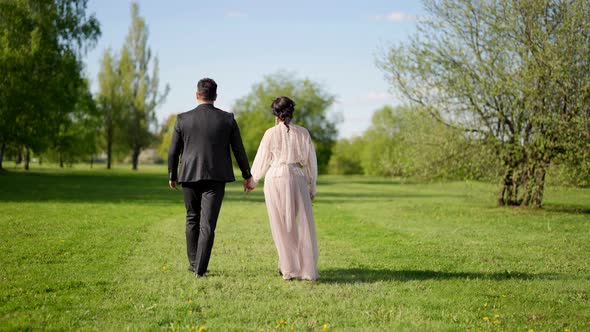Happy Loving Husband and Wife are Walking Together in Beautiful Sunny Garden in Spring Day Rear View alt