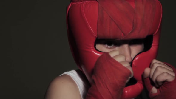 Young guy boxer in a protective stance looks at the camera. Red helmet on head