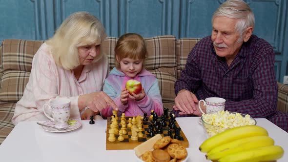 Senior Couple Grandfather Grandmother Resting on Sofa Playing Chess with Granddaughter Child Kid alt