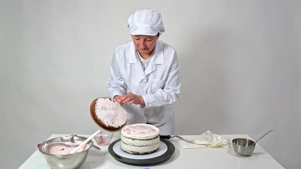A Baker Woman in a White Robe Puts the Last Layer of the Cake on the Sugar Cream alt