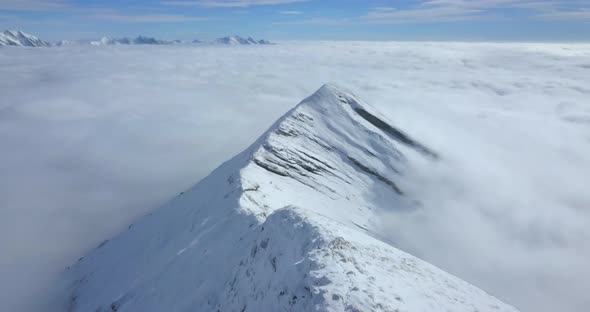 Aerial drone view above the clouds and snow covered mountains in the winter. alt