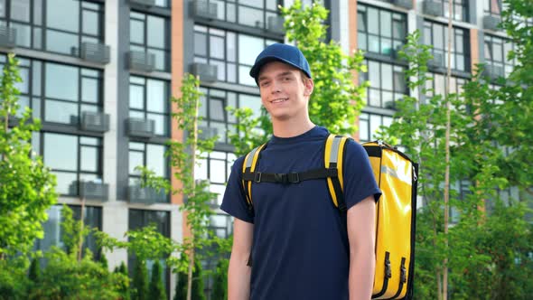 Smiling Man Courier Food Delivery with Backpack Turns Head and Looks Camera alt