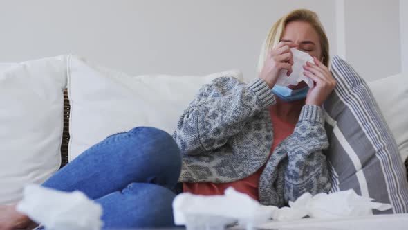 Sick woman with tissue sneezing while lying on couch at home alt