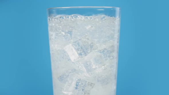 Glass Full of Cold Sparkling Water with Ice Cubes on Blue Background Transparent Fizzy Drink alt
