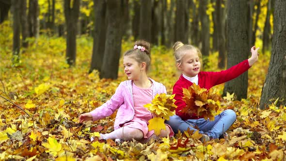 Two little girls collect a bouquet of yellow leaves in the autumn in the Park.