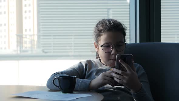 Little Girl Eating Cookies and Looking at a Smartphone alt
