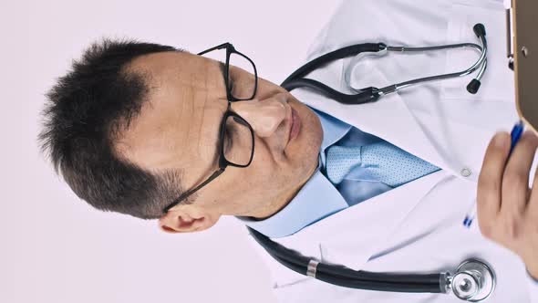 Vertical Shot Handsome Doctor Writes Prescription on Clipboard Looks at Camera with Smile