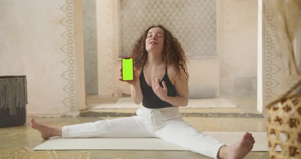 CurlyHaired Woman Fitness Coach Showing Exercises Online Using Smartphone with Green Screen