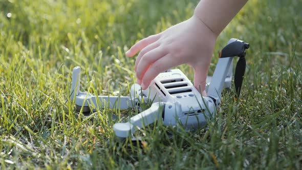 A Child's Hand Picks Up a Fallen Drone From a Green Lawn alt