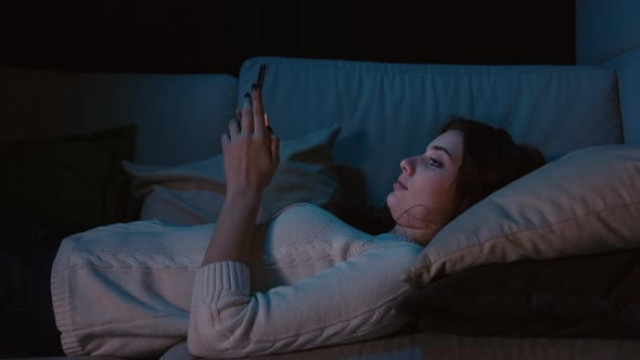 Millennial Woman Laying In Bed Holding Cellphone, Swiping Photos In Online Dating App  alt