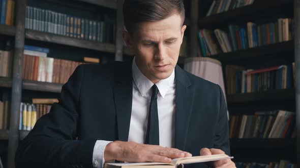 Young Man in Classical Suit Sitting in Library Searching for Information in Books