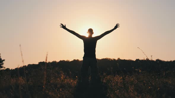 Silhouette of Young Man Against Sunset Raising Hands Sides and Up. Slow Motion alt