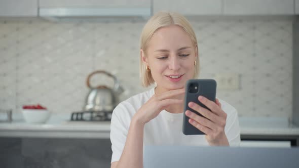 Attractive Blonde Woman Talks in Video Call While Sitting in Kitchen