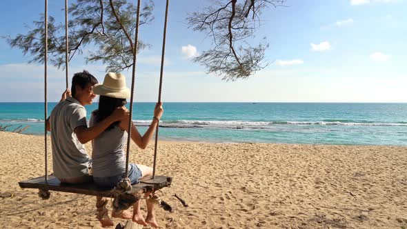 Happy Asian couple swinging on a swing at the beach during travel trip on holidays alt