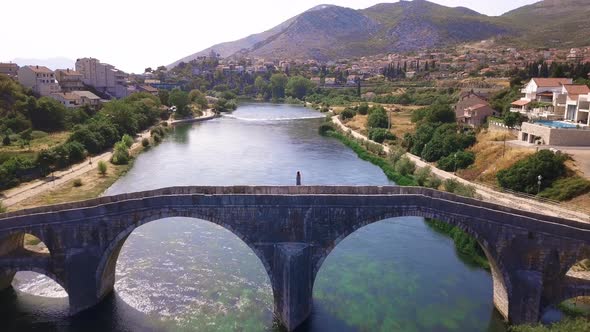 Lone girl in a traditional dress standing on the edge of a Arslanagic/Perovic bridge in Trebinje