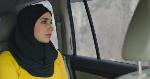 A Serious, Thoughtful Arab Woman in a Car in the Passenger Seat. Rides in the Car and Looks Out the alt