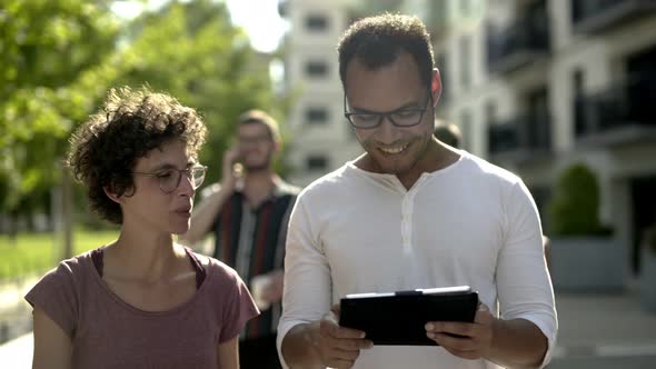 Smiling Couple in Eyeglasses Holding Devices on Street alt