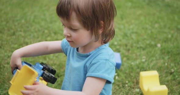 Cute Child is Playing with Toy Car and Cubes on Green Grass