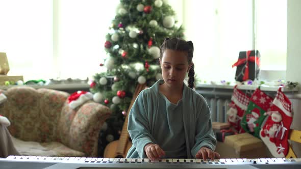 A Cute Little Girl Sitting Near a White Piano and a Christmas Tree