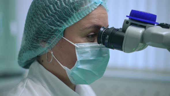Side View Headshot of Focused Professional Orthodontist at Dental Microscope with Light Flashing in alt