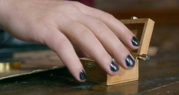 Person with Black Nail Polish on Nails Takes Small Music Box From Table to Listen to Uncomplicated