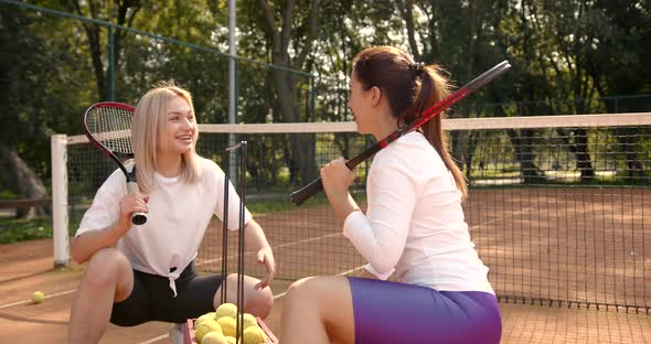 Two Young Women Sitting with Box for Tennis Balls