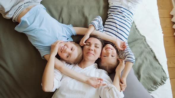 Happy Mother with Two Children Laying on Bed at Home Having Fun and Playing