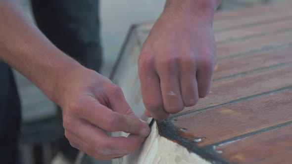 Cleaning scraping off excess sikaflex sealant on wooden boat cabin roof. Close up alt