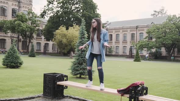 Stylish Cheerful Young Lady Dancing on a Bench with Earplugs on alt