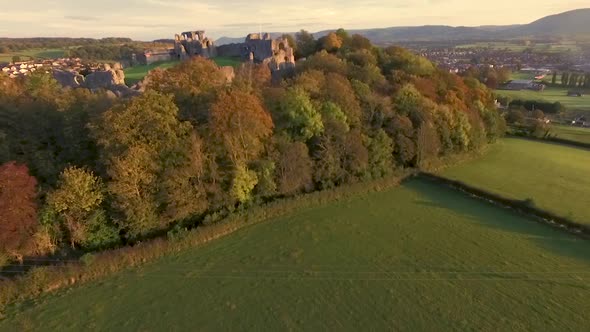 pan up revealing castle ruins sat on hilltop above village in welsh town alt