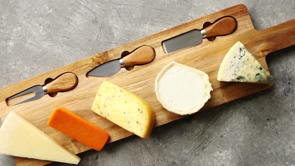Assortment of Various Kinds of Cheeses Served on Wooden Board with Fork and Knives alt