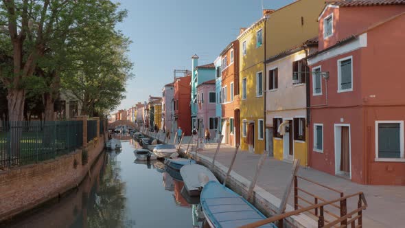 Waterside street with brightly painted houses and walking people Burano, Italy alt