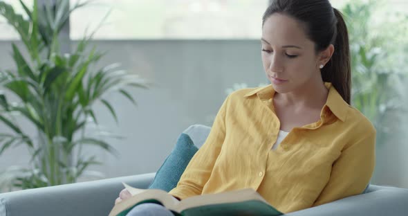Woman sitting on the armchair and reading a book alt