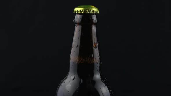 Drops of Condensate Flow Down a Beer Bottle on a Dark Background alt