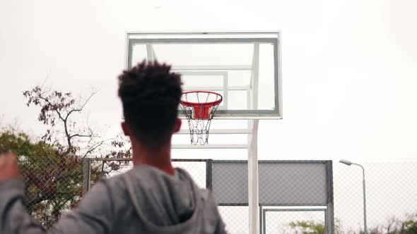 Young African Player Jumping Up and Throwing Ball in a Basketball Hoop the Ball Hits the Ring and alt